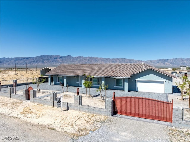 ranch-style house featuring an attached garage, a fenced front yard, a mountain view, and a tile roof