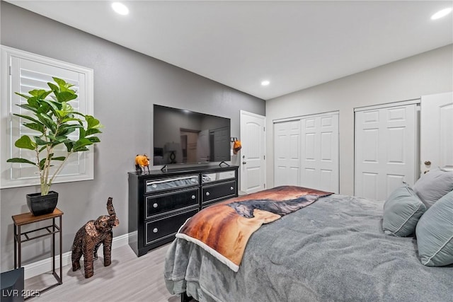 bedroom featuring recessed lighting, baseboards, wood finished floors, and two closets