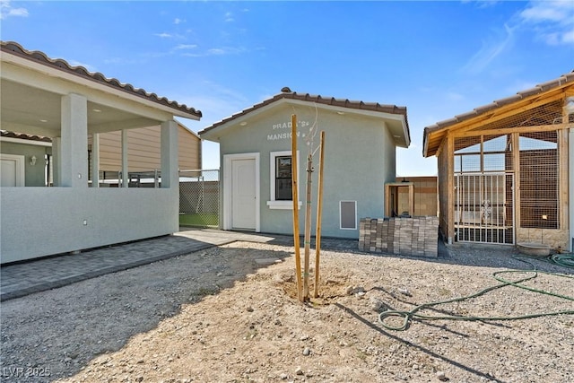 rear view of property featuring an outdoor structure, a tile roof, and stucco siding