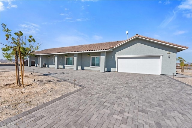 ranch-style house with decorative driveway, a garage, stucco siding, and a tile roof