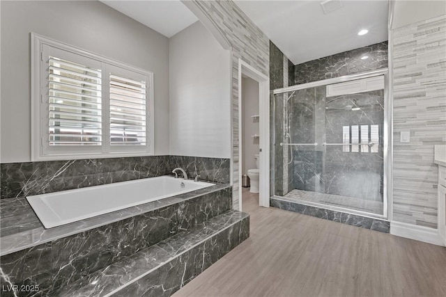 bathroom with a stall shower, toilet, a bath, and wood finished floors