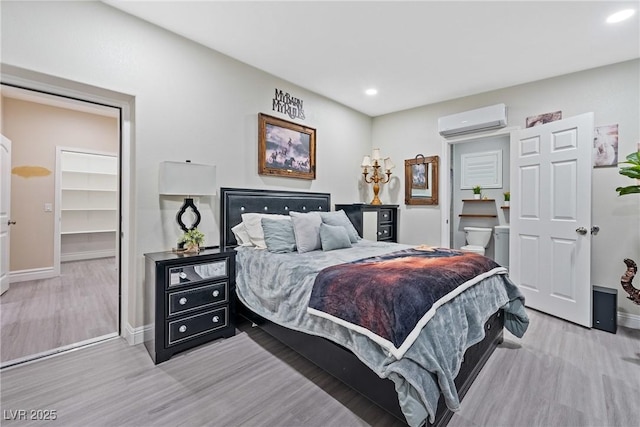 bedroom with a wall mounted air conditioner, baseboards, a spacious closet, recessed lighting, and light wood-style flooring