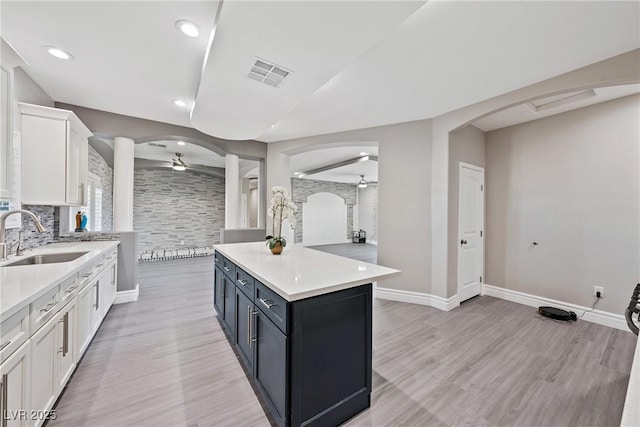 kitchen featuring a sink, a ceiling fan, white cabinets, and arched walkways