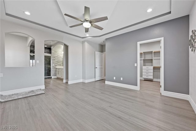 unfurnished living room with a ceiling fan, arched walkways, wood finished floors, and a raised ceiling