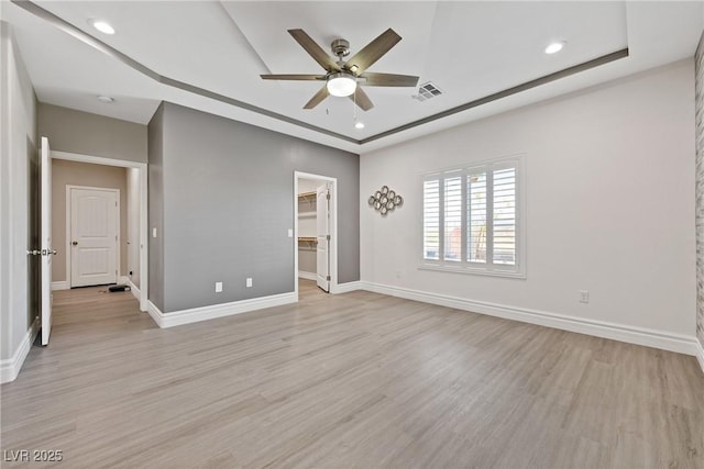 unfurnished room featuring visible vents, a raised ceiling, ceiling fan, and light wood finished floors