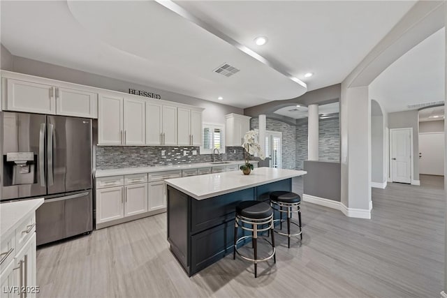 kitchen featuring a sink, light countertops, white cabinets, stainless steel fridge with ice dispenser, and arched walkways