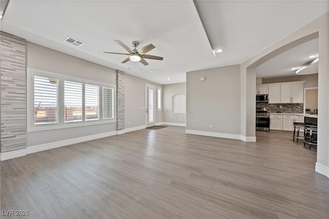 unfurnished living room featuring light wood-style floors, arched walkways, ceiling fan, and visible vents
