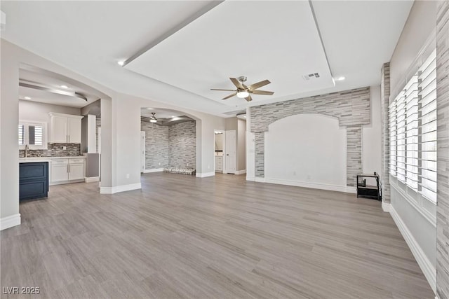 unfurnished living room with light wood-style floors, arched walkways, a ceiling fan, baseboards, and visible vents