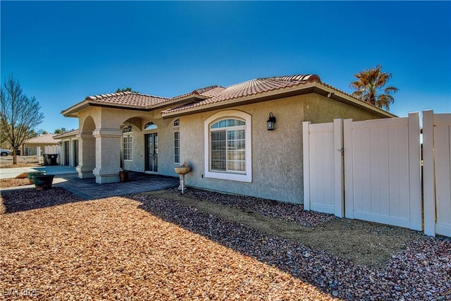 view of side of property with a tile roof, a gate, stucco siding, and fence