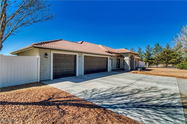 mediterranean / spanish home with fence, a garage, stucco siding, a tile roof, and driveway