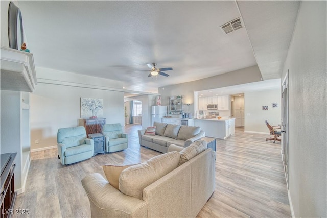 living area with baseboards, visible vents, light wood-type flooring, and a ceiling fan