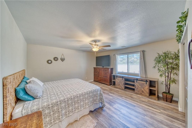 bedroom featuring a ceiling fan, wood finished floors, a textured ceiling, baseboards, and visible vents