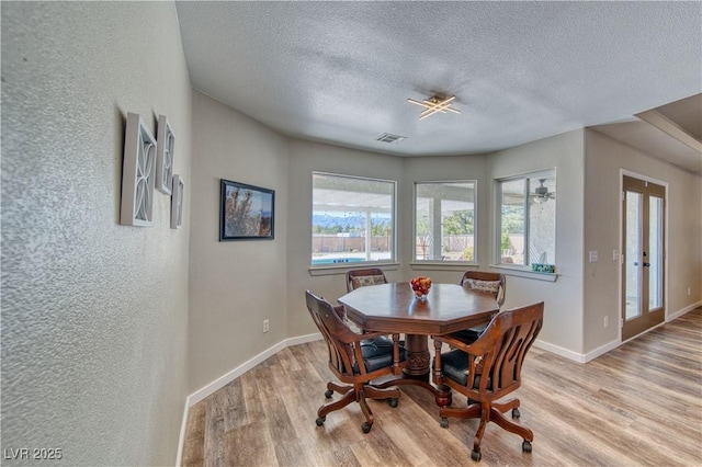 dining room with light wood finished floors, baseboards, visible vents, and a textured ceiling