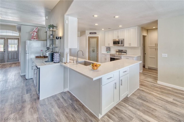 kitchen featuring a sink, white cabinetry, a peninsula, light wood-type flooring, and stainless steel appliances