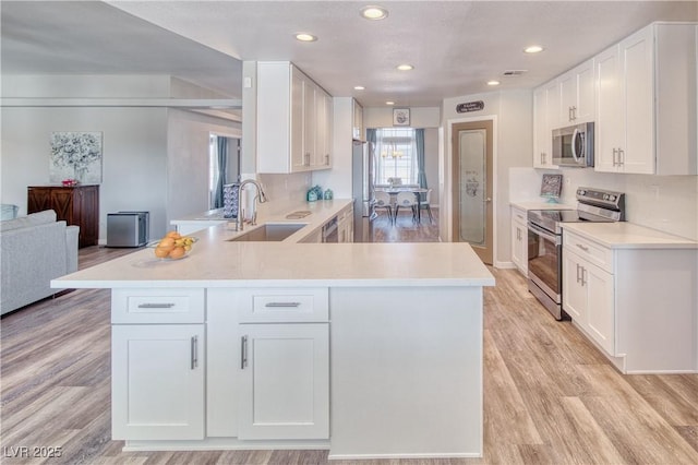 kitchen featuring light countertops, a sink, white cabinets, a peninsula, and appliances with stainless steel finishes