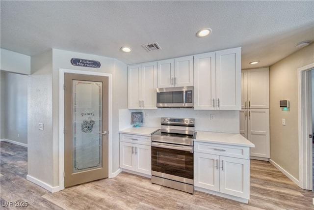 kitchen with white cabinets, visible vents, stainless steel appliances, and light countertops