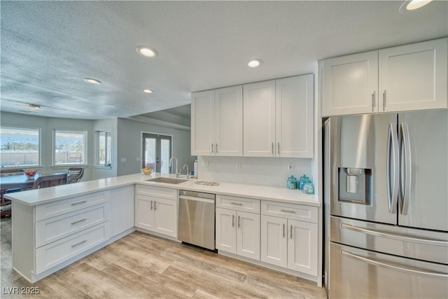 kitchen with white cabinetry, light countertops, stainless steel appliances, a sink, and a peninsula