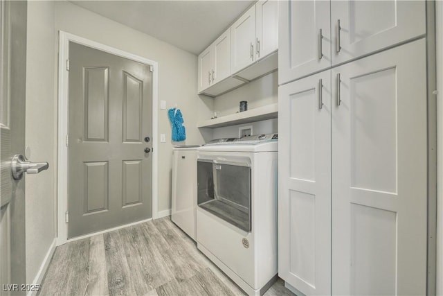 washroom with light wood finished floors, baseboards, washing machine and dryer, and cabinet space