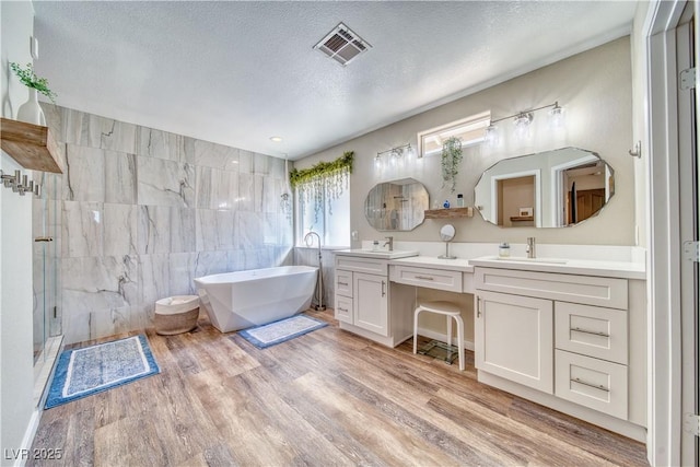 full bathroom featuring a textured ceiling, a sink, a stall shower, visible vents, and wood finished floors
