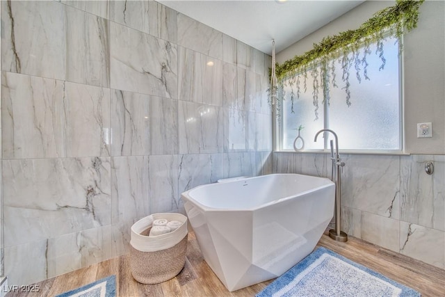 full bathroom with a freestanding bath, wood finished floors, and tile walls