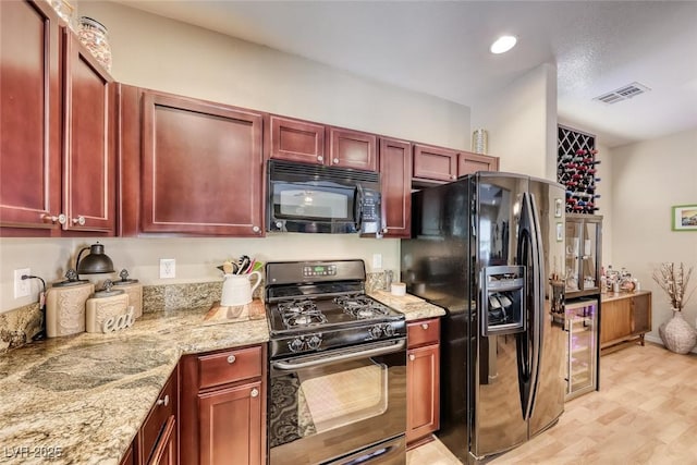 kitchen featuring reddish brown cabinets, black appliances, visible vents, and light stone counters