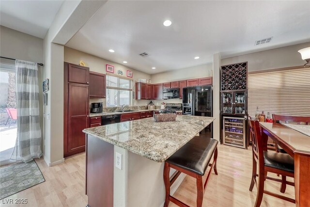 kitchen featuring light wood-type flooring, a center island, a sink, visible vents, and black appliances