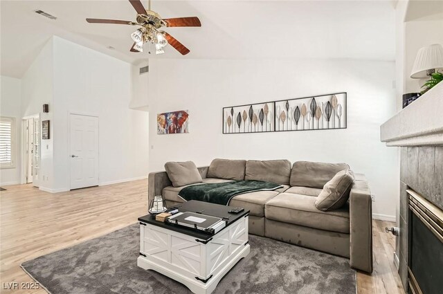 8515 Belcastro St, Las Vegas, NV 89113 - living area with a ceiling fan, light wood-type flooring, baseboards, a tiled fireplace, and high vaulted ceiling