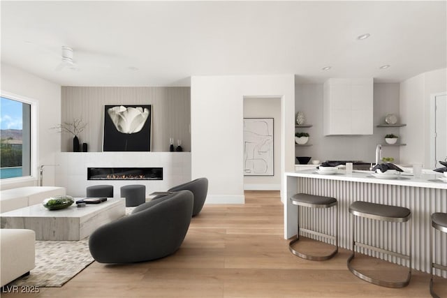 living room with a glass covered fireplace, baseboards, recessed lighting, and light wood-style flooring