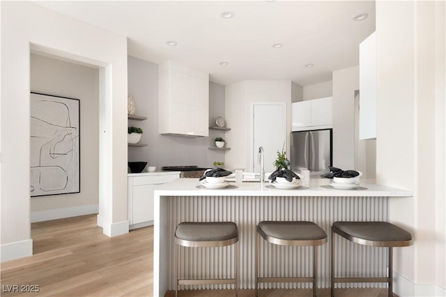 kitchen with freestanding refrigerator, a peninsula, a breakfast bar area, light countertops, and white cabinetry