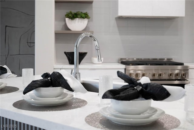 interior details with open shelves, a sink, light countertops, high end stove, and decorative backsplash