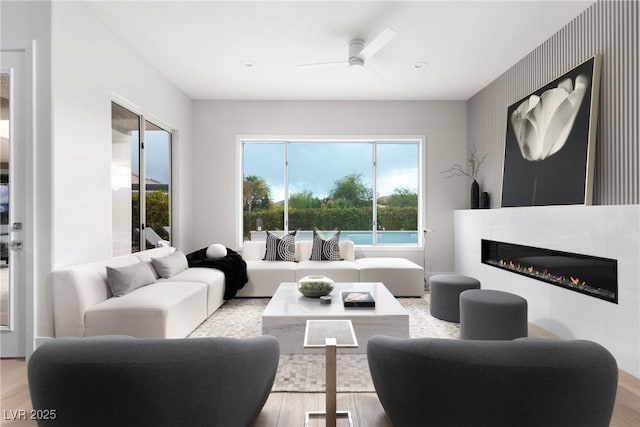 living area featuring a glass covered fireplace, a ceiling fan, and wood finished floors