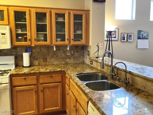 kitchen featuring a sink, tasteful backsplash, white appliances, stone countertops, and brown cabinets