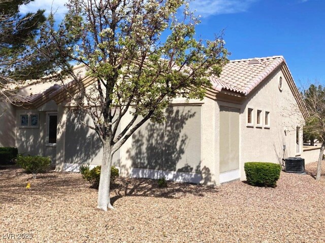 view of property exterior with a tile roof, cooling unit, and stucco siding