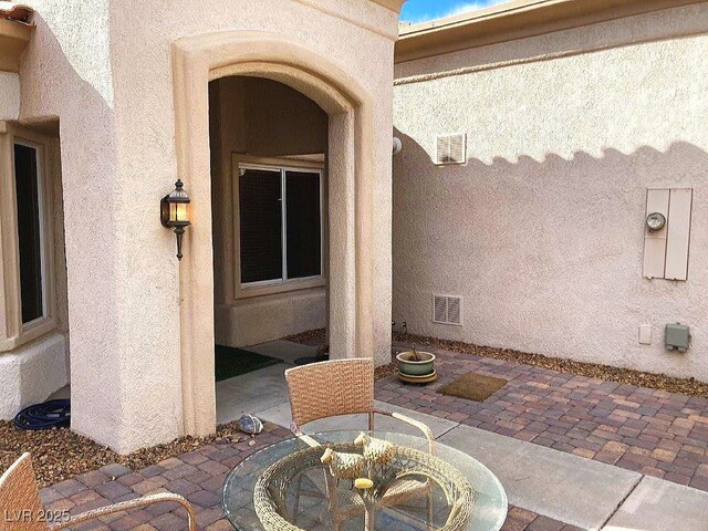 property entrance featuring stucco siding, visible vents, outdoor dining space, and a patio