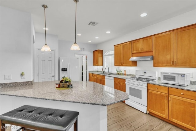 kitchen featuring white appliances, a sink, under cabinet range hood, a peninsula, and light stone counters
