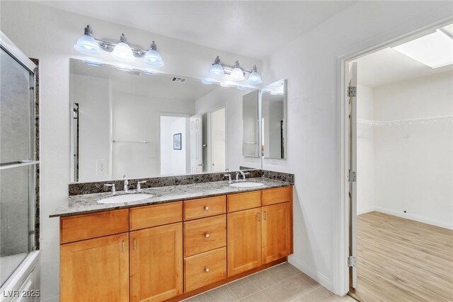 full bath with double vanity, a walk in closet, baseboards, and a shower with shower door