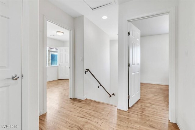 hallway with an upstairs landing, light wood-style flooring, baseboards, and attic access