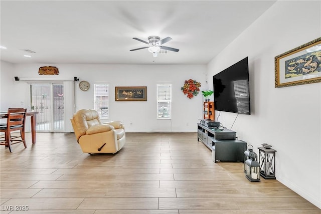 living room with healthy amount of natural light, ceiling fan, and light wood-style floors