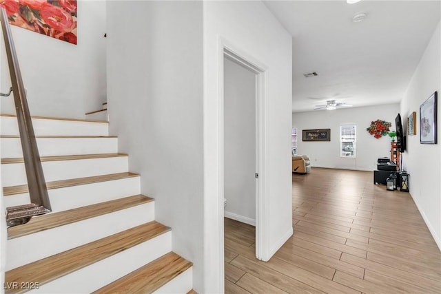 stairs with wood finished floors, baseboards, and a ceiling fan