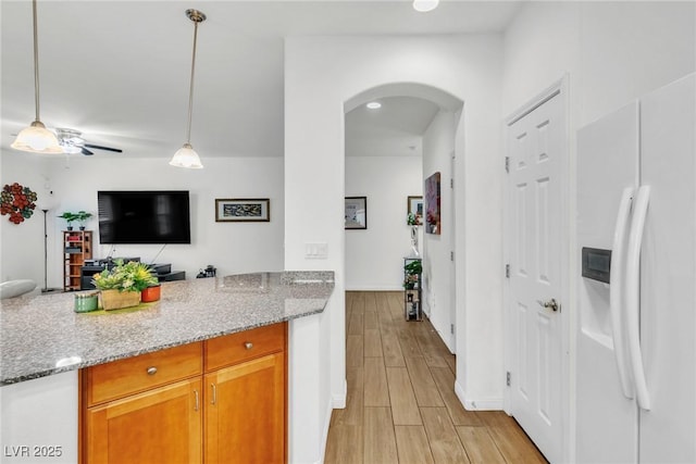 kitchen featuring white fridge with ice dispenser, arched walkways, open floor plan, and light stone countertops