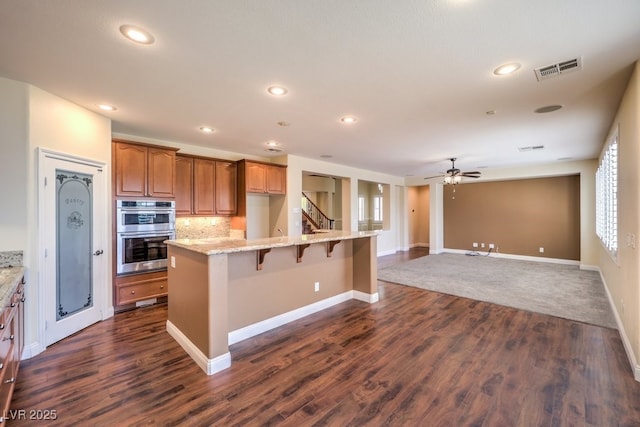 8429 Brackenfield Ave, Las Vegas, NV 89178 - kitchen with stainless steel double oven, dark wood finished floors, a kitchen bar, a ceiling fan, and light stone counters