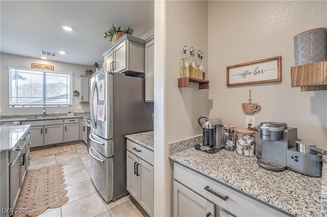 kitchen with light stone countertops, freestanding refrigerator, gray cabinetry, and visible vents