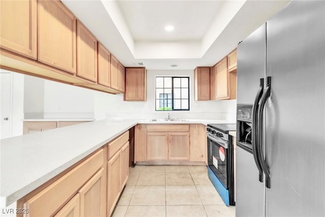 kitchen featuring a tray ceiling, stainless steel appliances, light brown cabinetry, a sink, and light tile patterned flooring