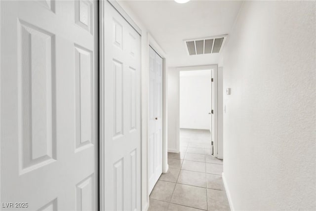 corridor with baseboards, visible vents, and light tile patterned floors