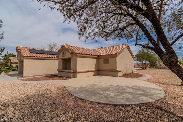 exterior space with a tiled roof, a patio, stucco siding, and roof mounted solar panels