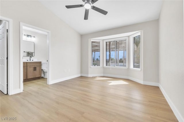 unfurnished bedroom with baseboards, light wood-type flooring, a sink, and vaulted ceiling