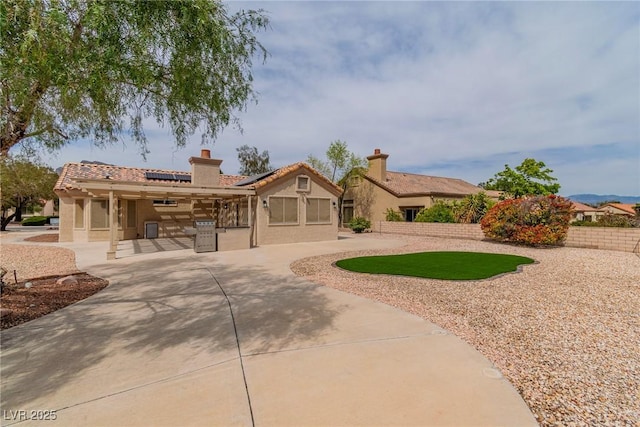 view of front of property featuring a tile roof, stucco siding, fence, roof mounted solar panels, and a chimney