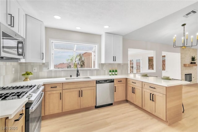 kitchen with a sink, a peninsula, light brown cabinets, stainless steel appliances, and an inviting chandelier