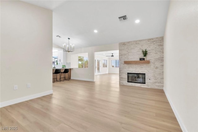 unfurnished living room with a stone fireplace, ceiling fan with notable chandelier, light wood-style floors, and visible vents
