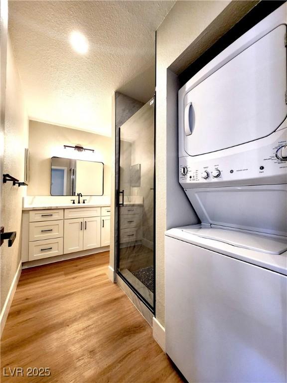 4050 Pacific Harbors Dr Unit 209, Las Vegas, NV 89121 - laundry room with a textured ceiling, stacked washer / dryer, light wood finished floors, baseboards, and a sink